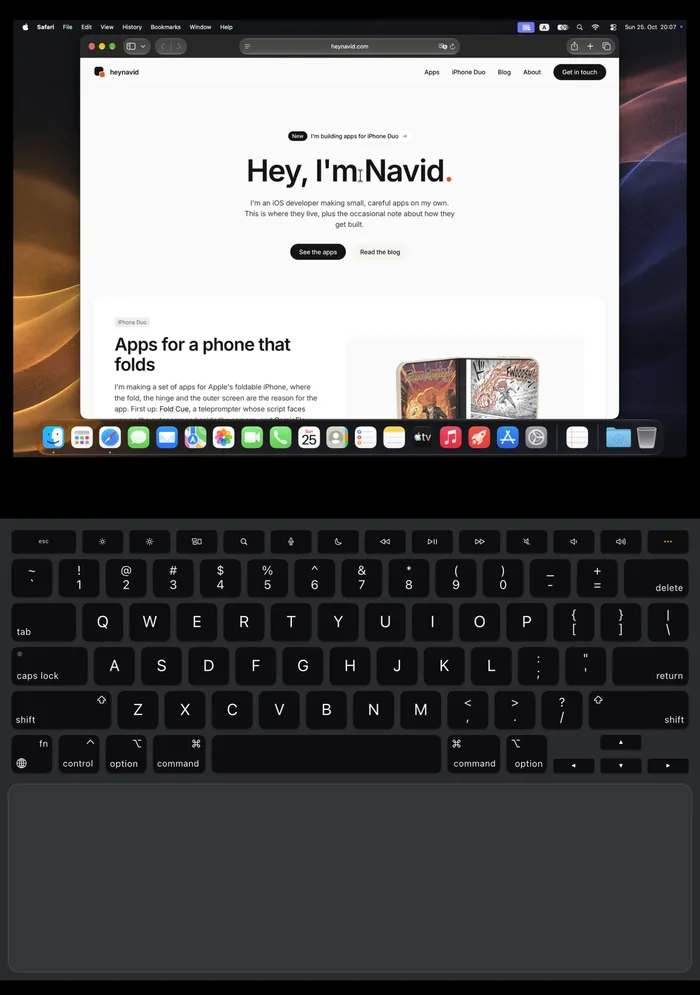Uplid on the iPhone Duo inner screen in laptop pose: a Mac desktop with Safari open on heynavid.com above the fold, the Mac keyboard and trackpad below it
